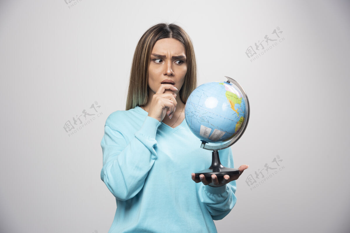 地理穿着蓝色运动衫的金发女孩手里拿着一个地球仪 仔细地思考着 努力地记住目的地摆姿势休闲