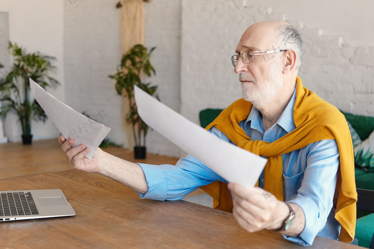 咖啡60多岁的悲伤男工程师 穿着正式的衣服 戴着眼镜 坐在木制办公桌旁 手里拿着普通的笔记本电脑 手里拿着文件 感到沮丧工作 职业和压力概念商人担心科技