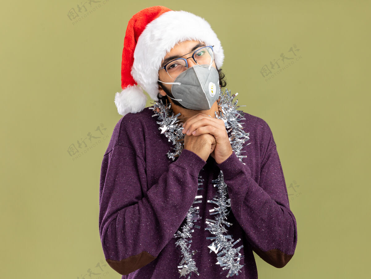 脖子年轻帅哥戴着圣诞帽 戴着医用面具 脖子上戴着花环 手牵着手 在橄榄绿的背景下与世隔绝花环医学圣诞