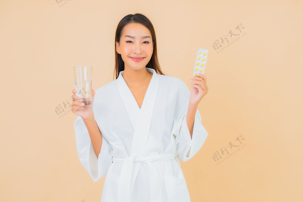 疾病一幅美丽的亚洲年轻女子的画像 米色的水杯和药丸女性医药胶囊