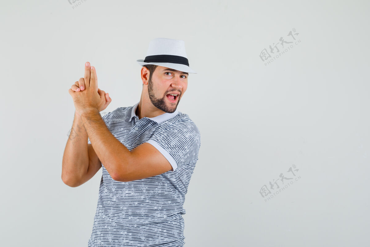 成人一个年轻人穿着t恤衫 戴着帽子 展示着手枪的姿势 看上去像个心形狮 正前方的视图空间为文本帽子休闲肖像