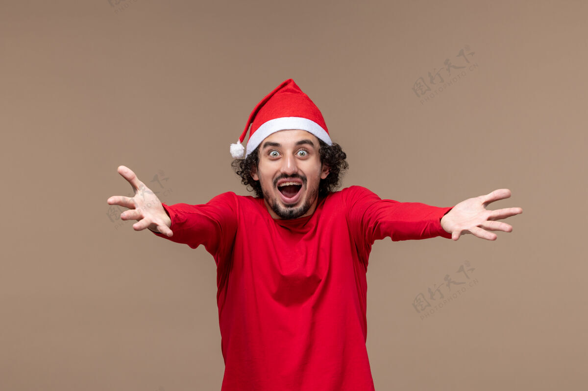 帽子正面图红色的男性在棕色背景上情绪化地摆姿势节日情绪圣诞节男人圣诞节微笑