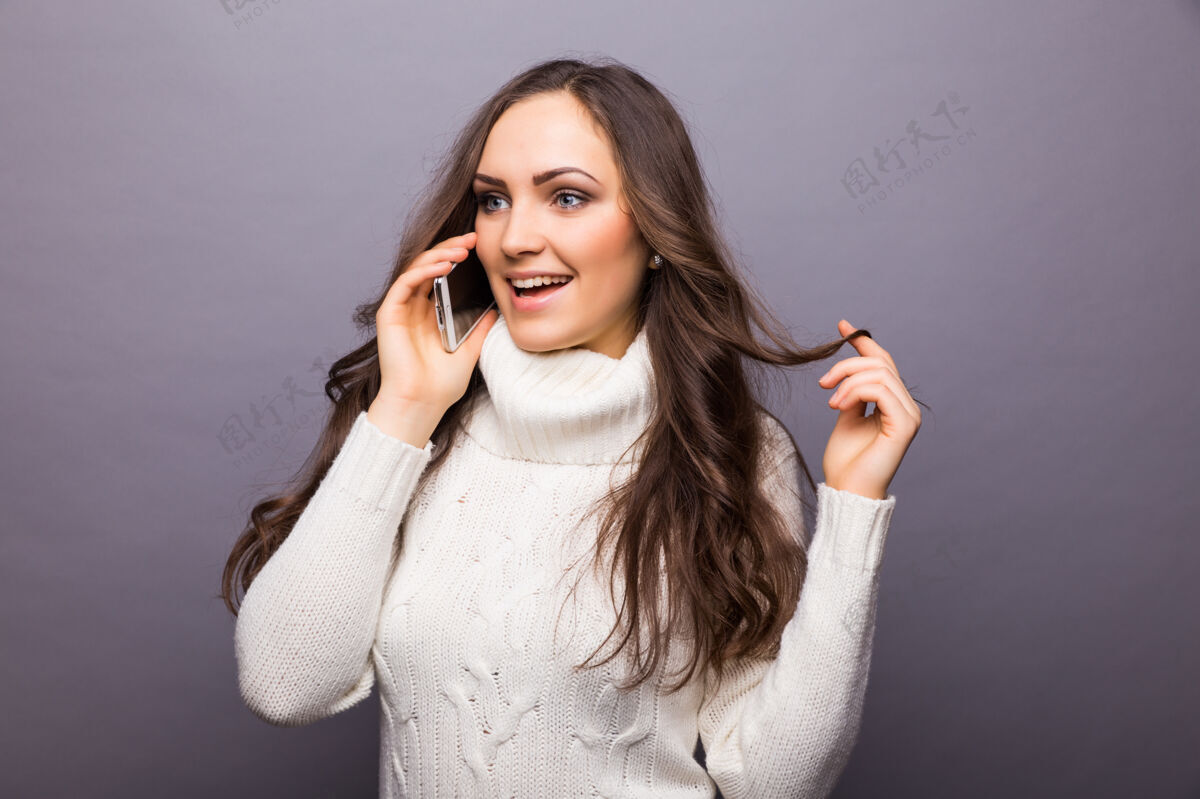 漂亮有趣的照片是一个戴着眼镜的年轻女子笑着用手机聊天 上身越过灰色的墙壁通话年轻表情