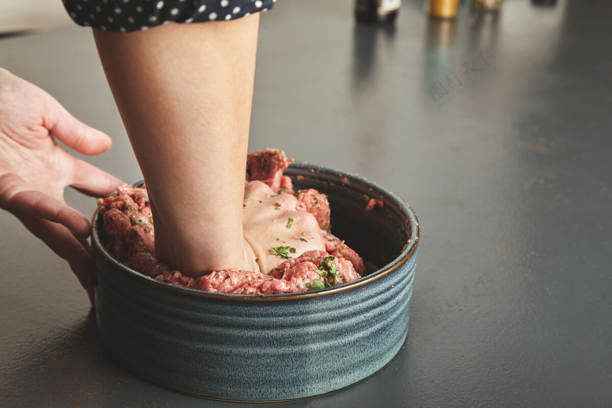 切碎的在蓝色的木桌上 女人们用手在陶瓷碗里揉肉末和香料牛肉带血的膳食