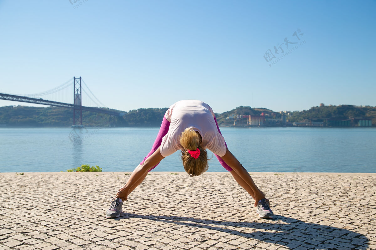 60岁穿着运动服的成熟女性在户外做早操 在河里伸展背部和腿部肌肉活动或积极的生活方式理念全长银行完整