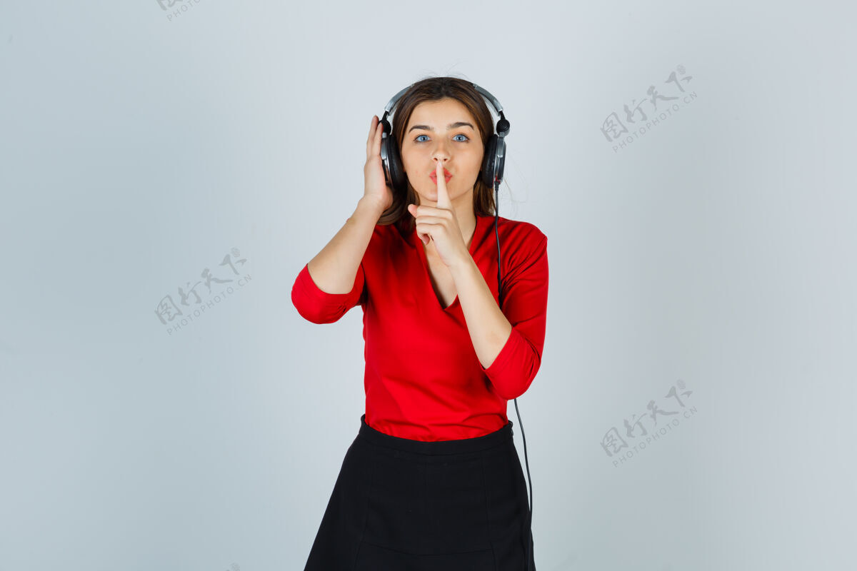 年轻戴着耳机的年轻女士一边听音乐 一边穿着红色上衣做着沉默的手势成人展示衬衫