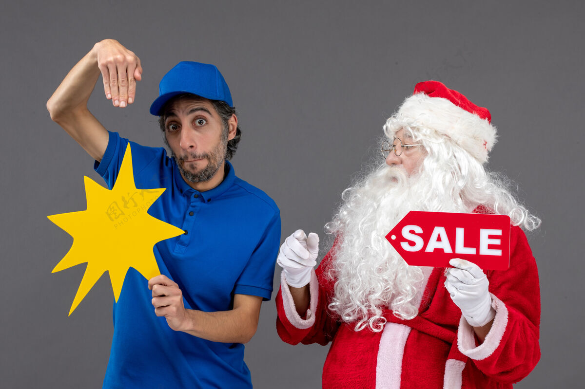 快乐圣诞老人的正面图 男性信使手持销售横幅 灰色墙上有黄色标志圣诞老人圣诞销售