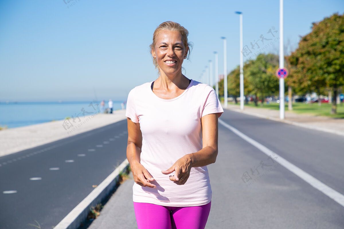 运动快乐的成年女性慢跑者在河边的跑道上走着 看着并指着手指正面视图活动和年龄概念活跃积极手指