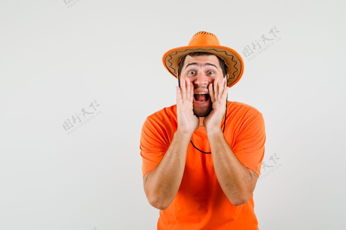 年轻年轻人穿着橙色t恤 戴着帽子 兴高采烈地喊着或宣布着什么正视图人男人工作室