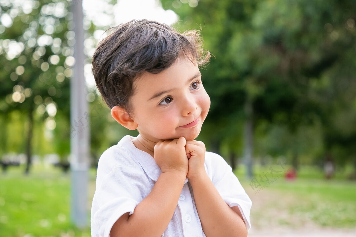 小快乐可爱的小男孩站在夏日公园里摆姿势 下巴靠在手上 微笑着看着别处特写镜头童年的概念黑发户外乐趣
