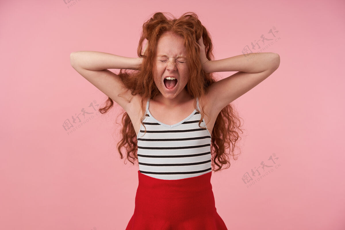 女学生横向拍摄的haywire长发卷发女孩穿着红色裙子和条纹上衣举着头 手掌抬高 闭着眼睛大声尖叫 隔离在粉红色背景上情绪欧洲封闭