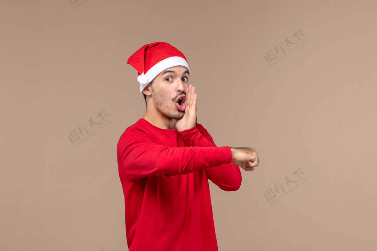 成人正面图：在棕色背景上穿着红色圣诞斗篷的年轻男性 喜怒哀乐微笑肖像快乐