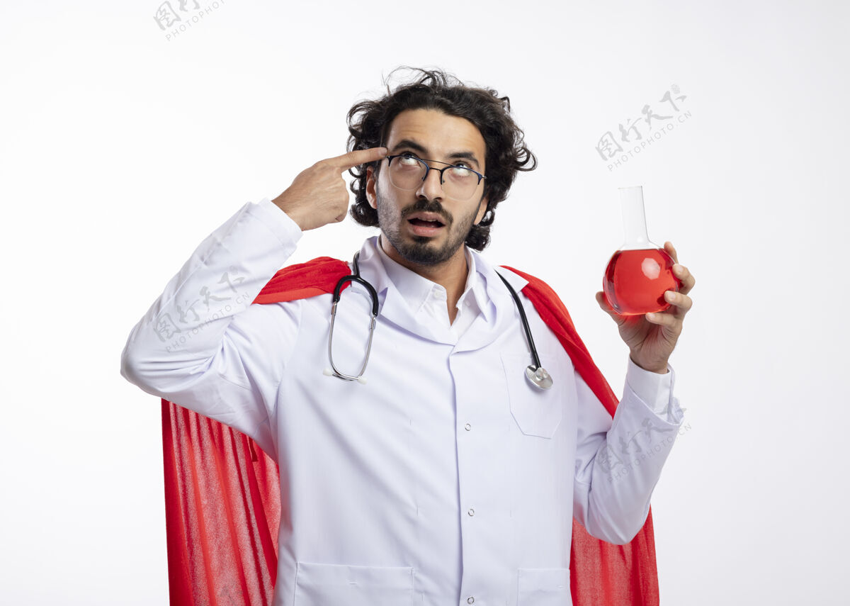 手指一个戴着眼镜 身穿医生制服 身穿红色斗篷 脖子上戴着听诊器的白人年轻人把手指放在太阳穴上 把红色的化学液体放在玻璃瓶中印象深刻放化学品