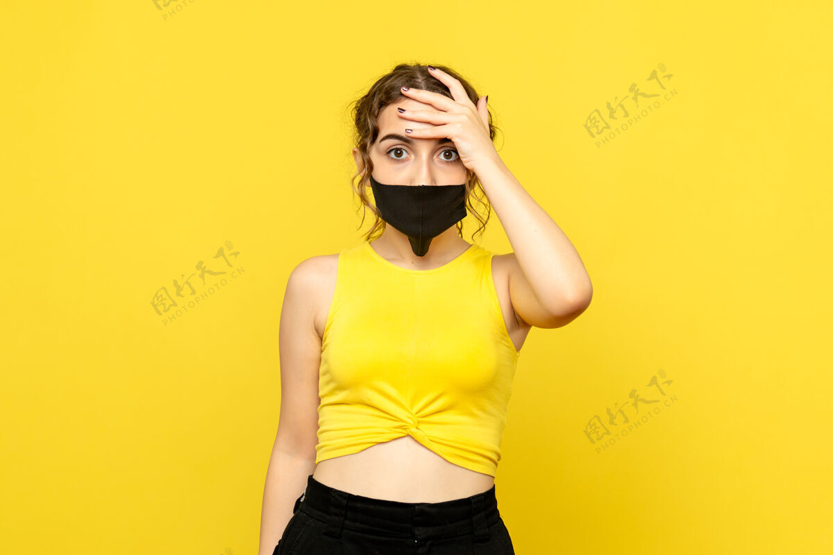 人物黄墙上戴着黑面具的年轻女子的正视图漂亮面具身体