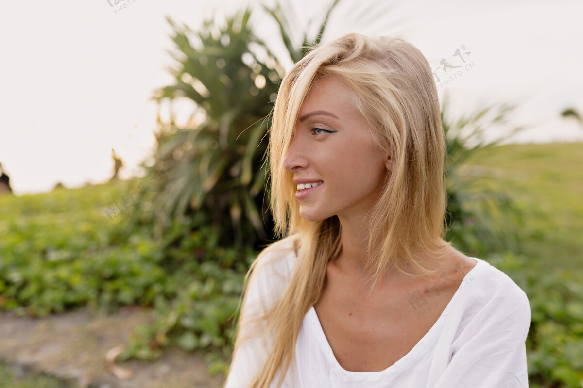 迷人美丽的20多岁的欧洲女人的肖像 留着长发 穿着夏天的白色连衣裙 一边笑着 一边看着远处 一边走在海边的沙滩上女孩肖像年轻