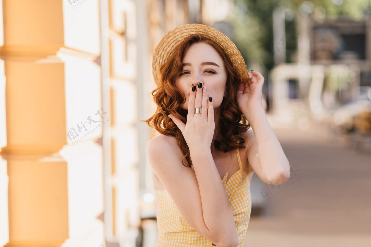 模特穿着黄色衣服的姜黄色迷人女孩在夏天的照片中送空气吻嬉皮的红发女人戴草帽表达爱的户外镜头配件公园城镇
