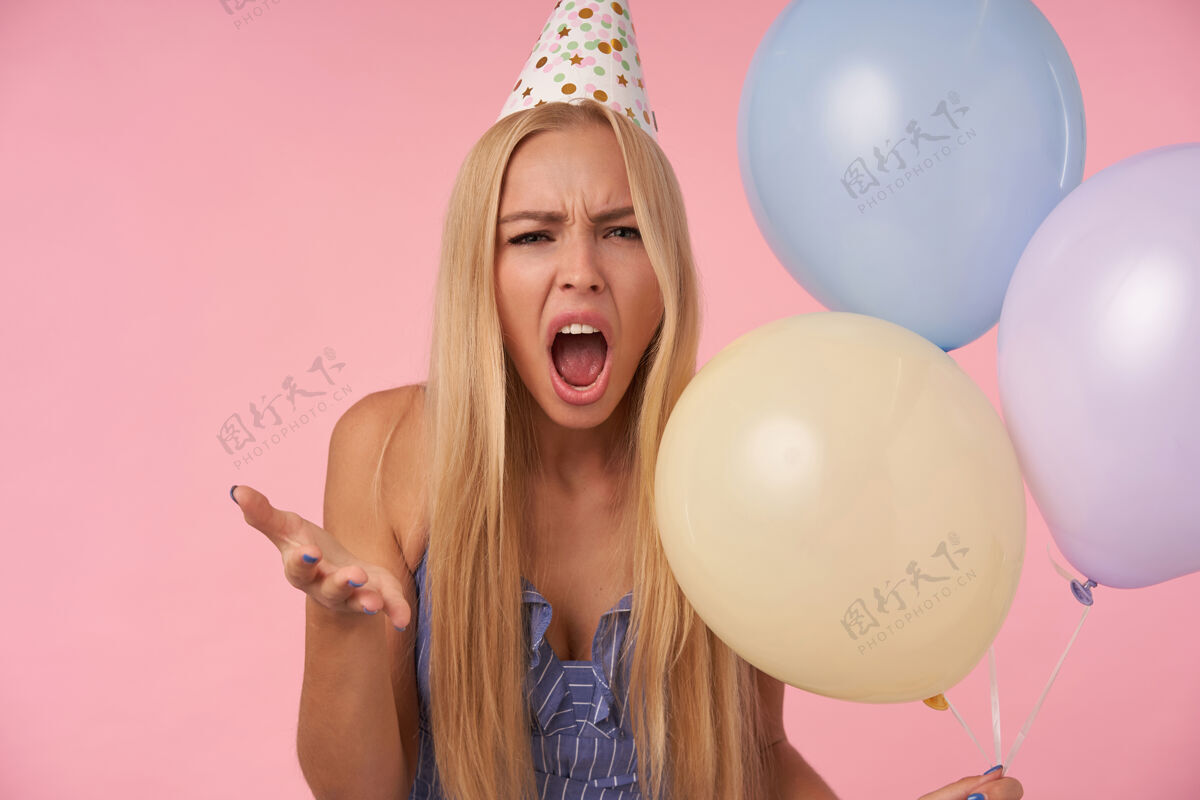 条纹严肃的年轻金发女性愤怒地举起手掌 张大嘴巴看着相机 精神不好 拿着一堆氦气球在粉色背景上摆姿势休闲发型庆祝