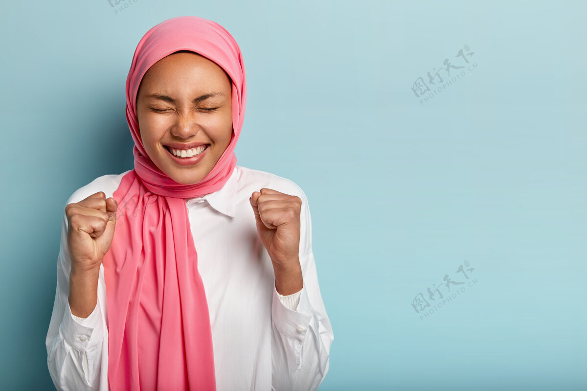 人类开心的阿拉伯女人举起拳头 成功进球 闭上眼睛穆斯林姿势满意