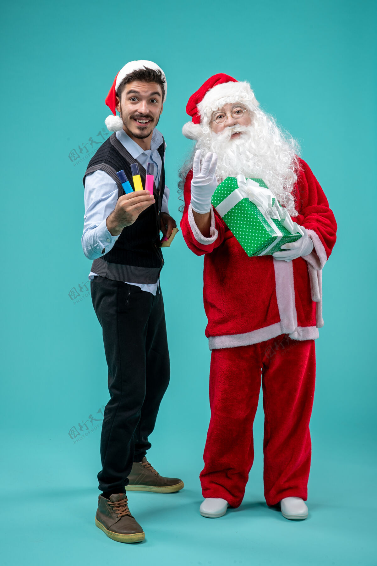 男性圣诞老人与年轻人和节日礼物在蓝色墙上的正面视图礼物微笑圣诞
