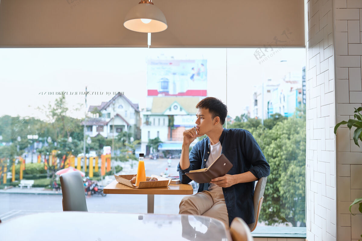 专业商人在咖啡馆窗口的笔记本上写字 专注于工作 自信的年轻人一边坐在咖啡馆里写字一边在笔记本上工作 年龄20-30岁食物桌子咖啡