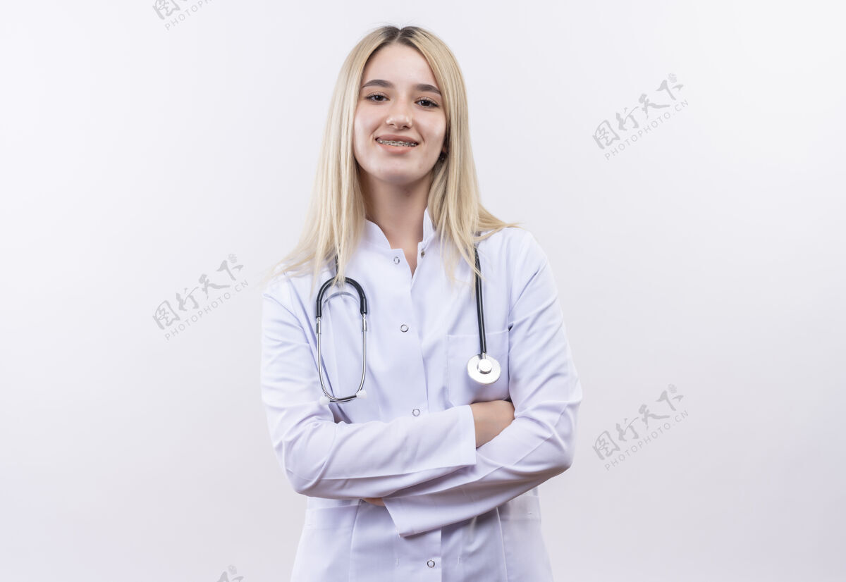 手微笑的医生年轻的金发女孩戴着听诊器和医用长袍戴着牙套双手交叉在孤立的白色背景上医生牙科年轻