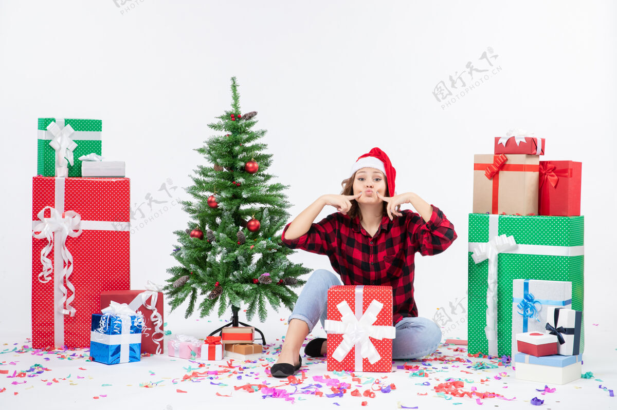 坐年轻女子围坐在圣诞礼物和白色墙上的小圣诞树前的视图十二月圣诞快乐节日
