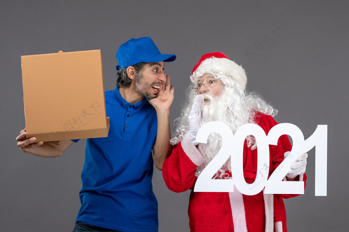 圣诞老人圣诞老人的正面图 男信使拿着食物盒 站在灰色的墙上帽子庆祝圣诞快乐