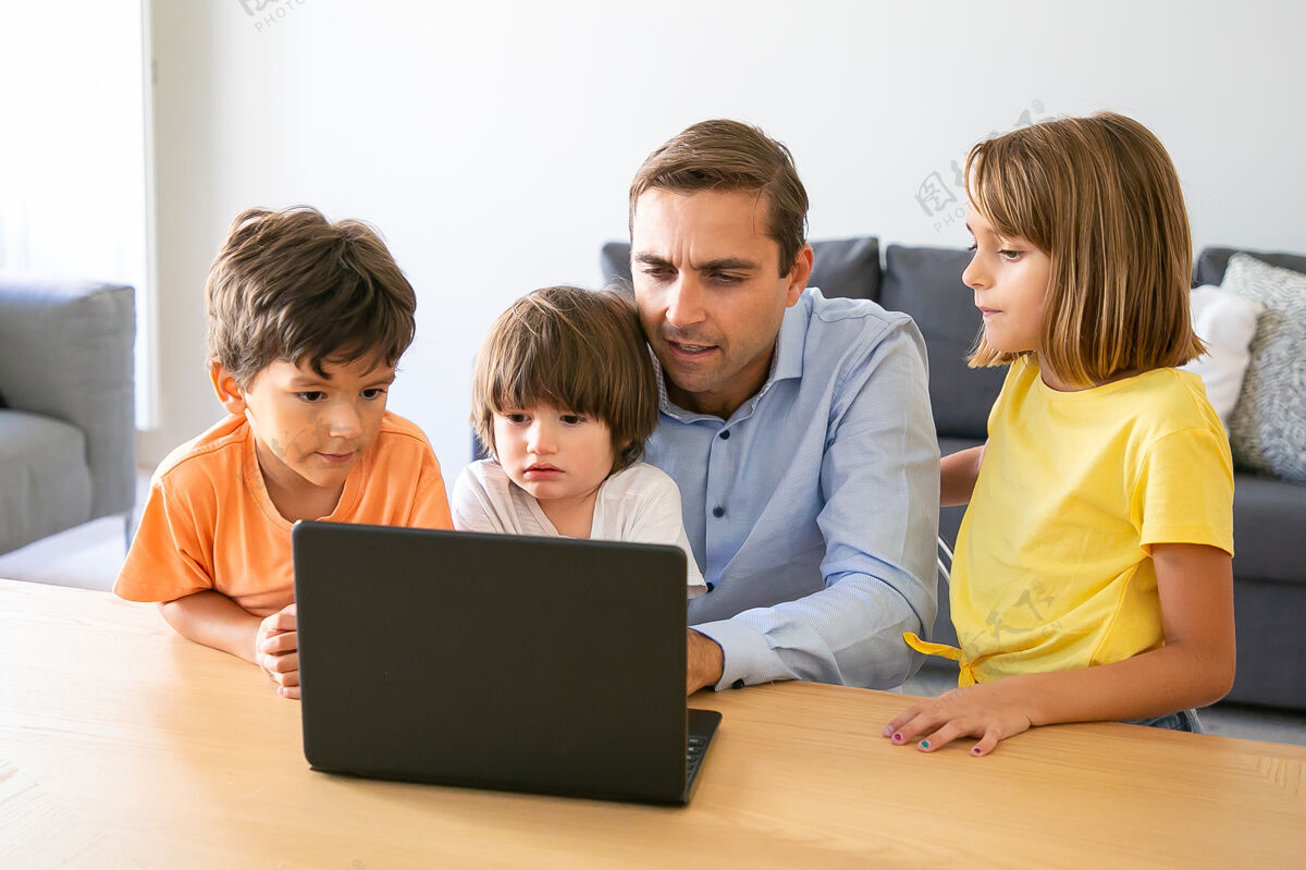 笔记本电脑沉思的父亲和孩子们在笔记本电脑屏幕上看一些东西专注的白人父亲坐在桌子旁 周围都是可爱的孩子童年 家庭 父亲和数字技术的概念孩子数码可爱