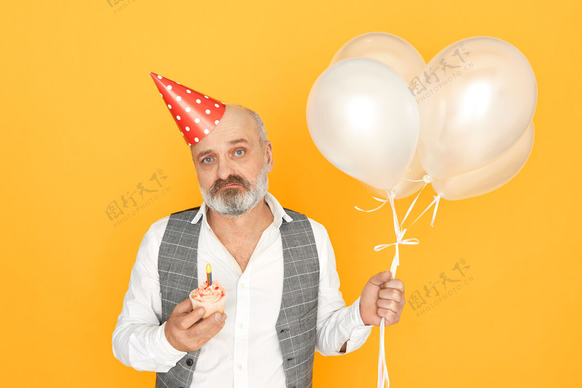 愿望孤零零的一张照片 照片上是一个不快乐的男性退休者 秃顶上戴着圆锥形帽子 情绪低落 老了 手里拿着气球和纸杯蛋糕欢乐肖像退休