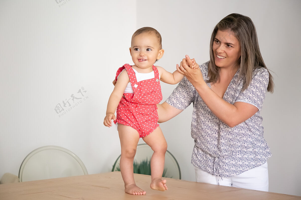 童年快乐的宝宝穿着红色的身体 牵着妈妈的手 试图走在桌子上全长父母和童年的概念父母可爱可爱