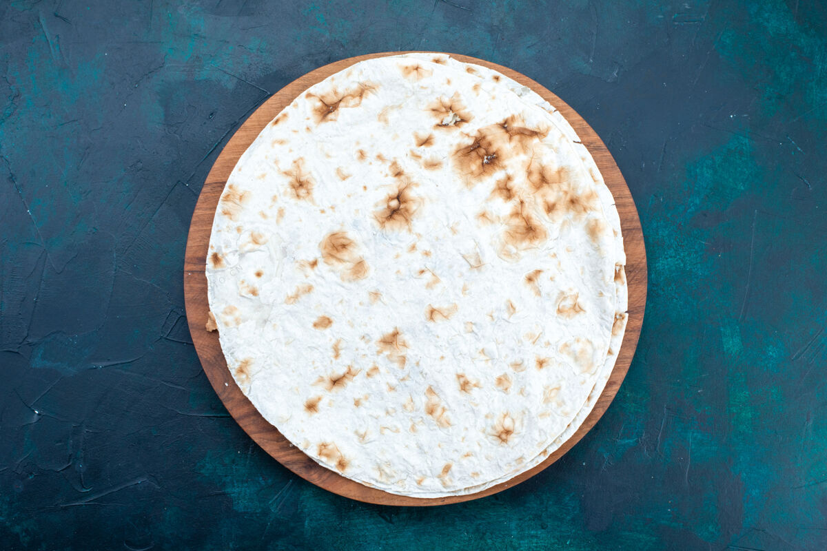 生面团在深蓝色表面上的圆形普通皮塔面包状面团俯视图脸粉食物粉