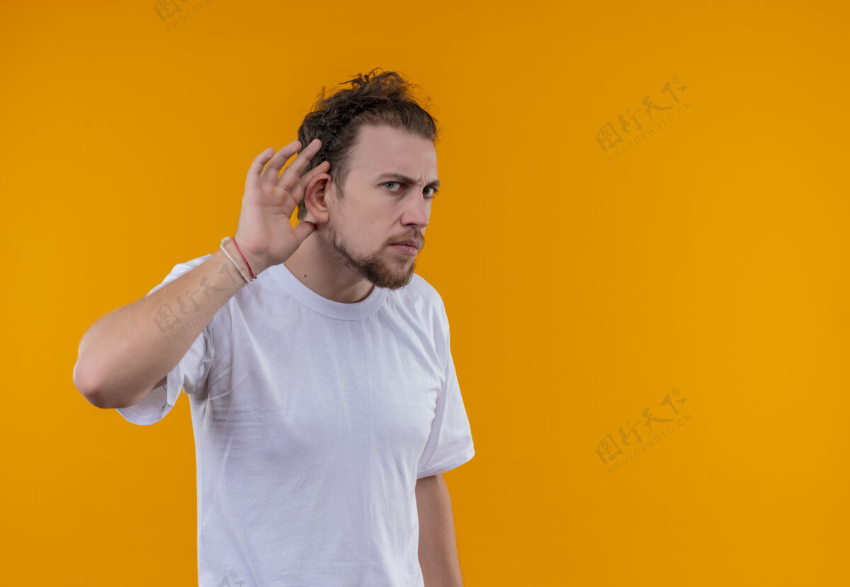 男人看起来年轻人穿着白色t恤 在孤立的橙色背景上显示倾听手势看橙色穿