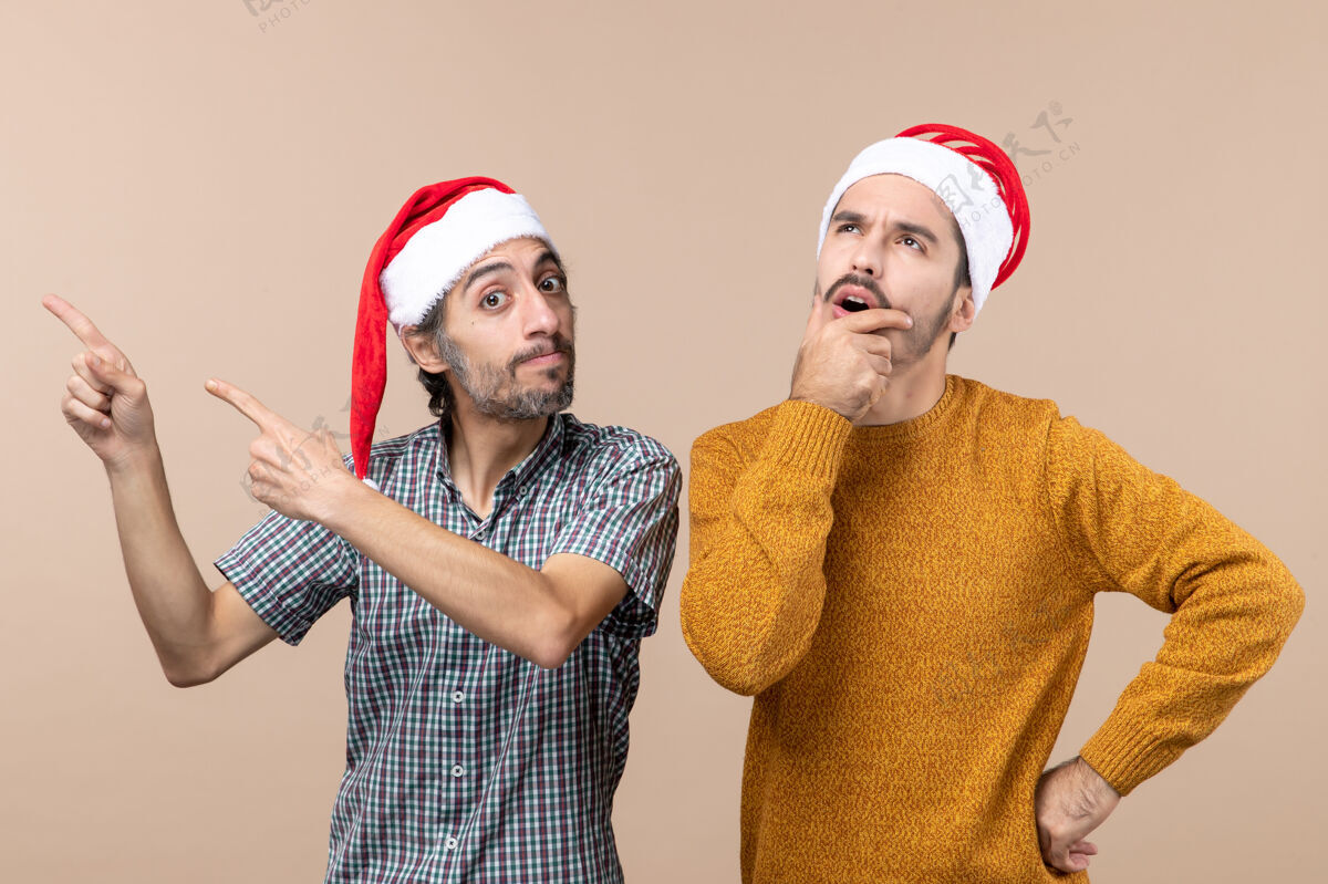成人正面图两个戴着圣诞帽的家伙 一个在展示什么 另一个在思考 手放在嘴上 背景是米色的男人手米色