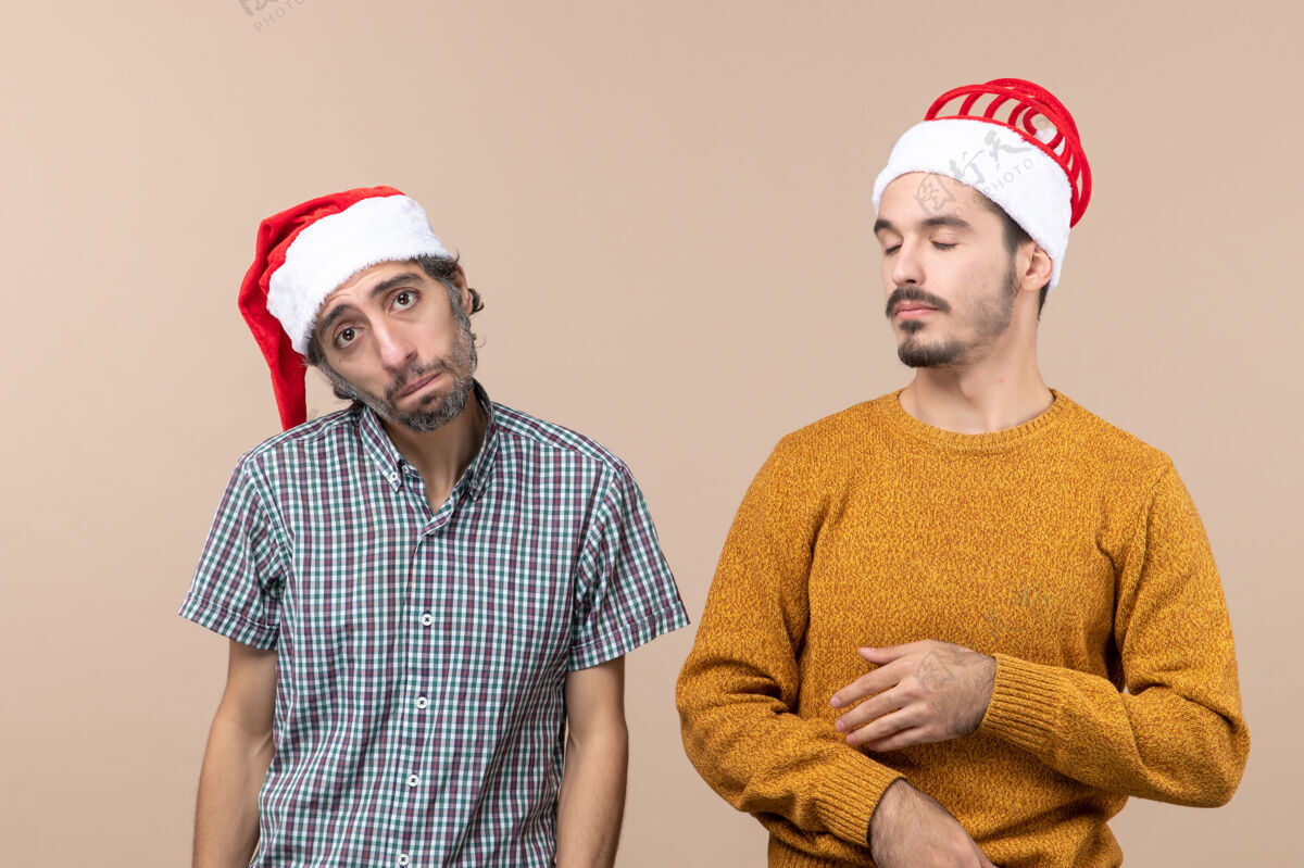 圣诞老人前视图两个家伙一个沮丧的和一个昏昏欲睡的圣诞老人帽子在米色孤立的背景两个前面男人