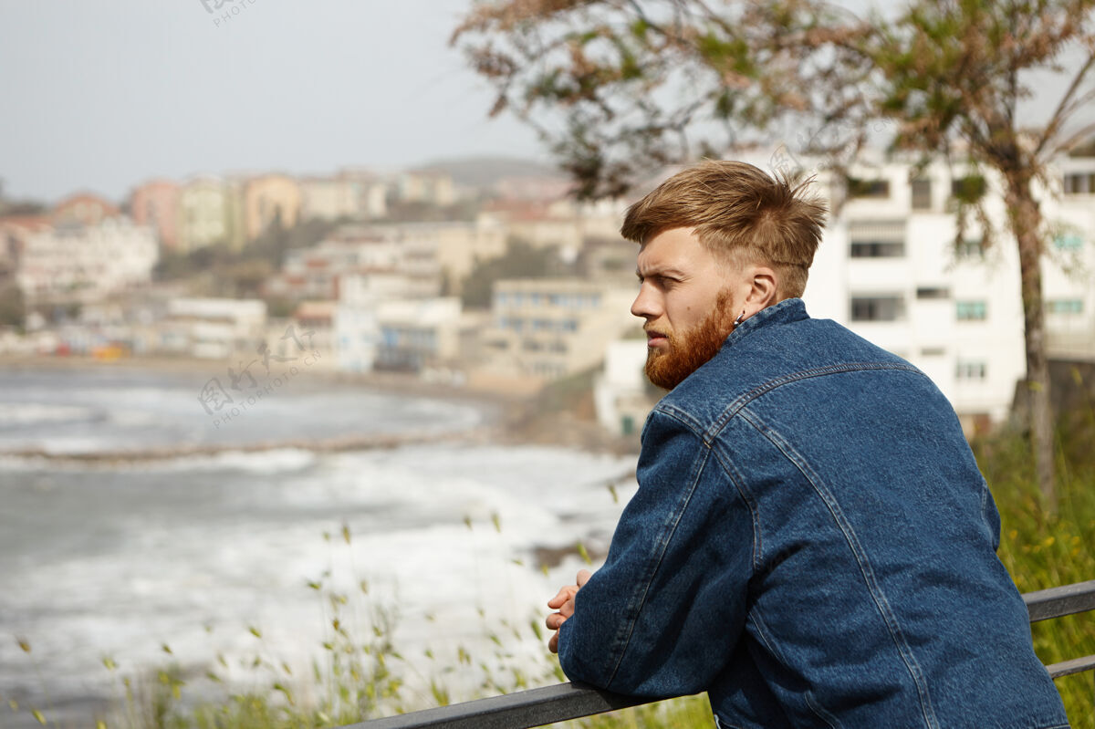 水平迷人体贴的年轻欧洲男性 留着姜黄色长胡子 在户外摆姿势长凳海海洋