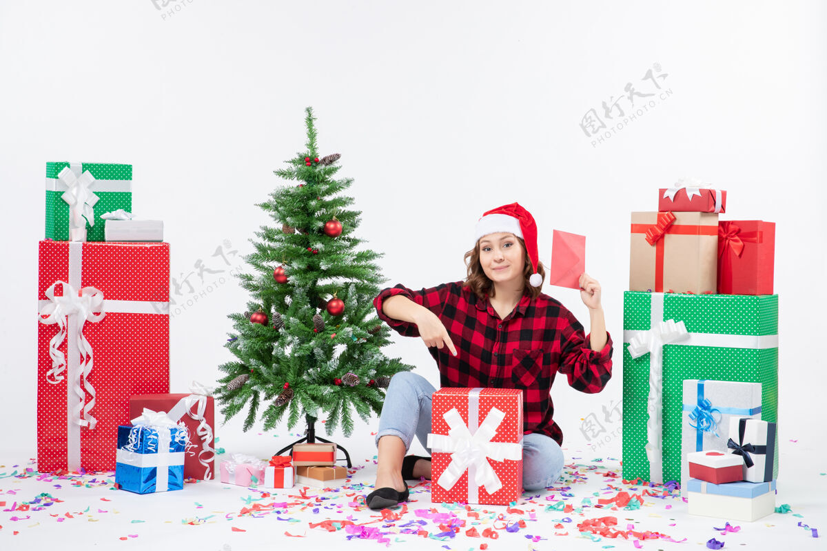 礼物前视图年轻女子坐在周围的礼物举行信封上的白墙人冬天情感