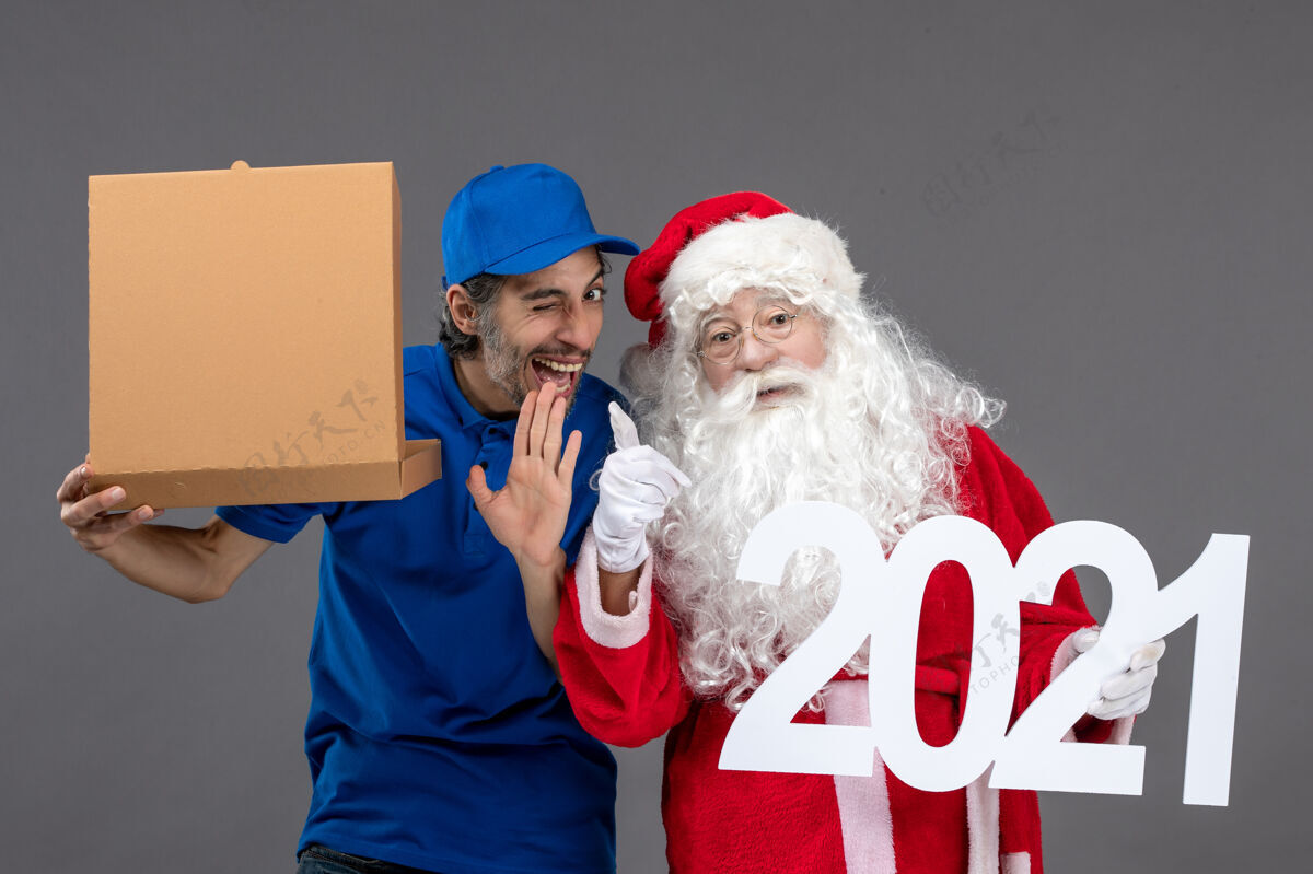庆祝圣诞老人的正面图 男信使拿着食物盒 站在灰色的墙上快乐圣诞老人人