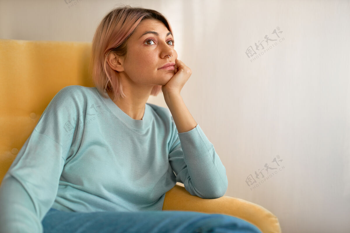 柔软无聊的年轻女性的画像 粉红色的鲍勃发型 坐在家里的黄色沙发上 手放在脸颊下休闲休息休息