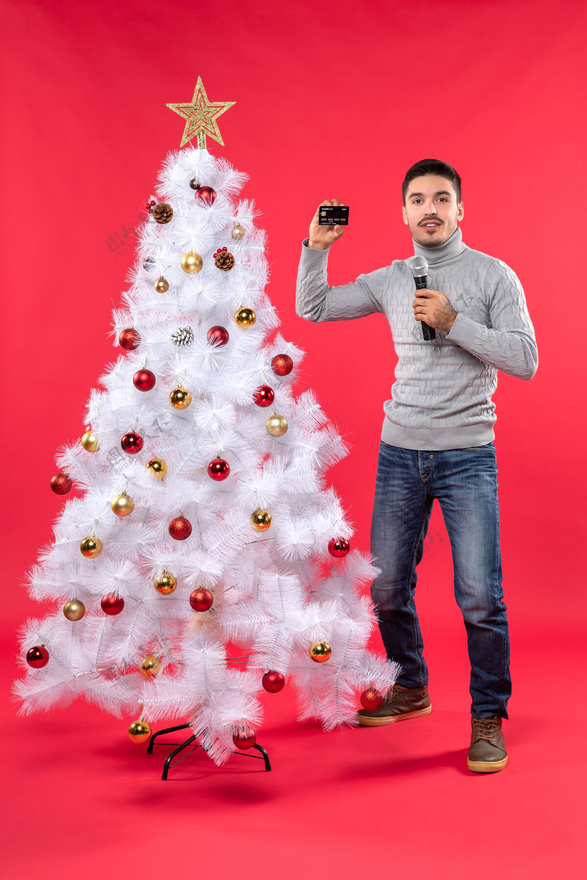 装饰圣诞节心情自信的家伙站在装饰好的圣诞树旁 拿着麦克风拍照自信圣诞树举行