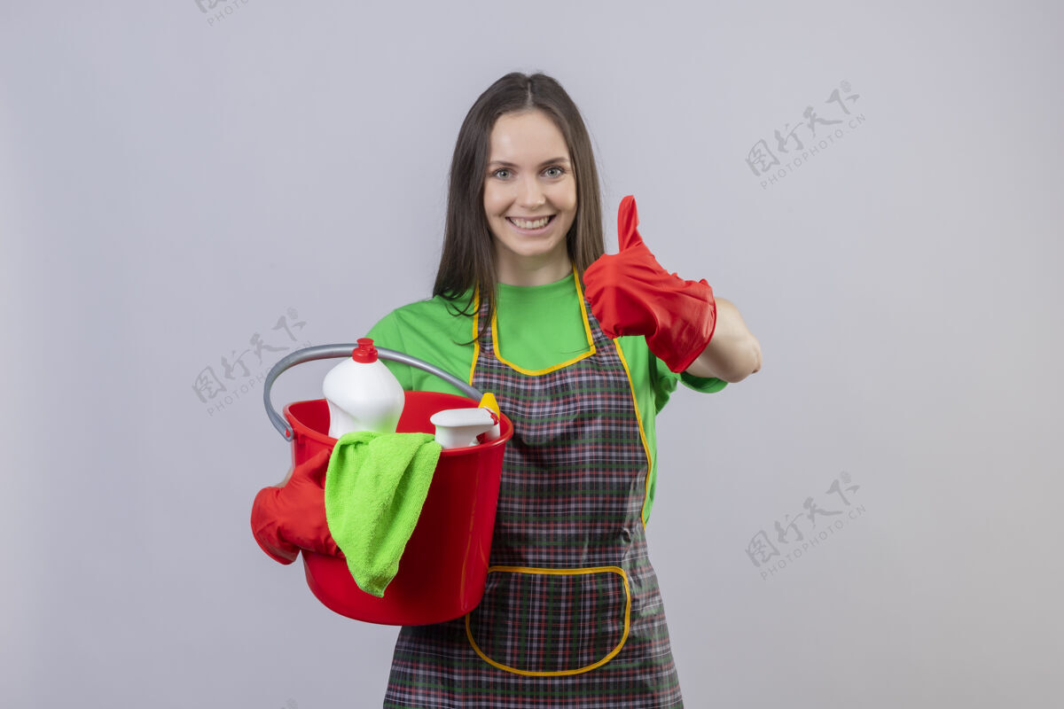微笑微笑着清洗穿着制服 戴着红手套 拿着清洁工具的年轻女孩 在孤立的白色背景上竖起大拇指工具女孩拇指