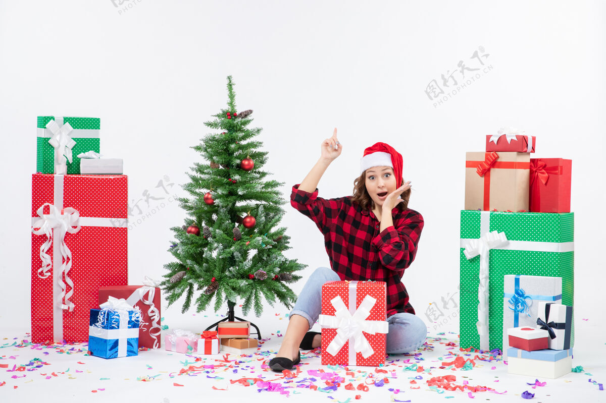 圣诞年轻女子围坐在礼物和白色墙上的小圣诞树前的视图装饰节日圣诞树