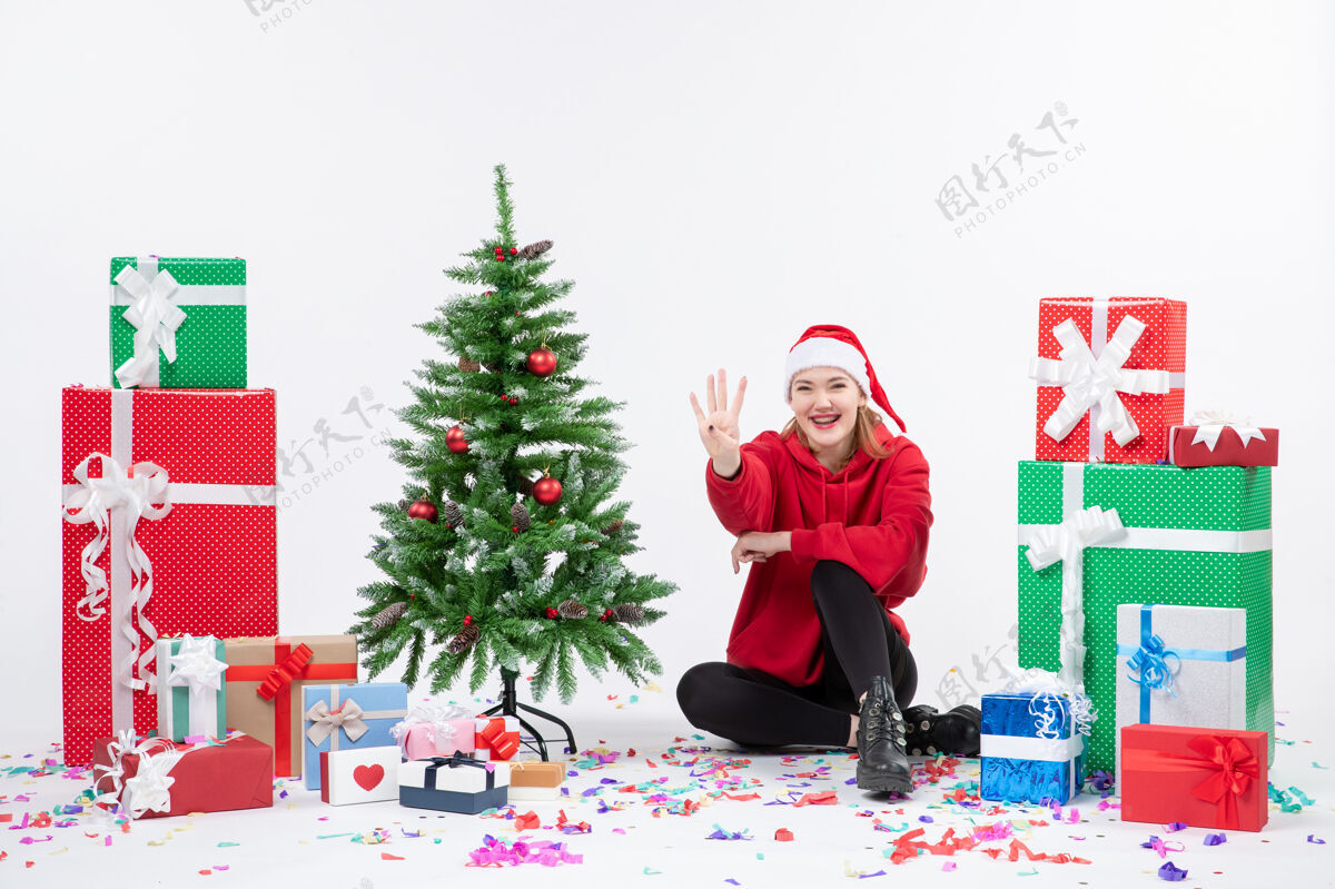 树年轻女子坐在白色墙壁上数着节日礼物的前视图圣诞节日雪