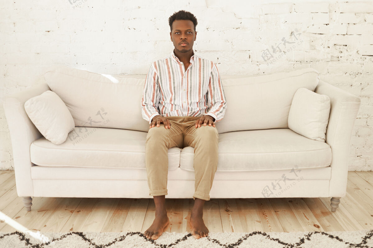 周末家 舒适和家庭生活的概念严肃的年轻非洲裔美国男性赤脚坐在客厅的沙发上放松男人休闲