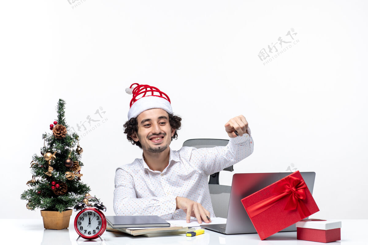 微笑微笑着的年轻商人戴着滑稽的圣诞老人帽 在白色背景的办公室里检查书写笔记和庆祝圣诞节圣诞老人支票帽子