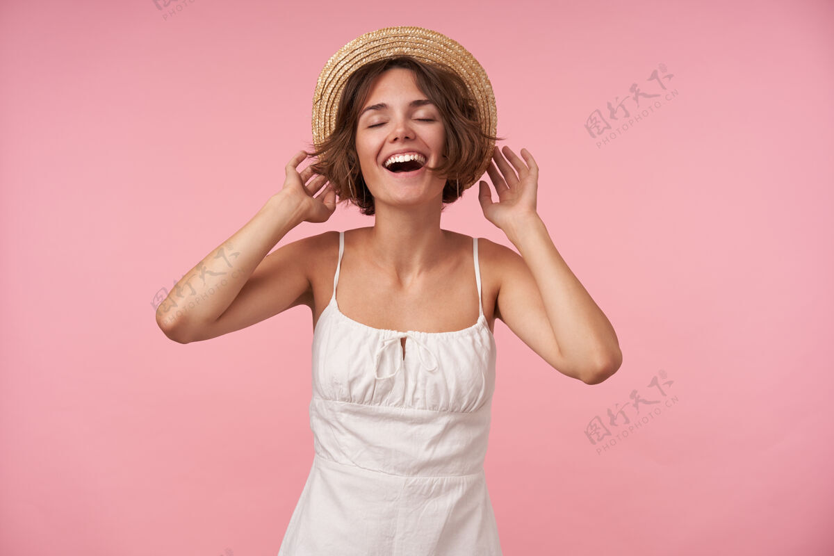 成人美丽的年轻女性 穿着白色的带肩带的夏装 头戴水手帽 闭着眼睛摆姿势 精神饱满微笑站着情绪