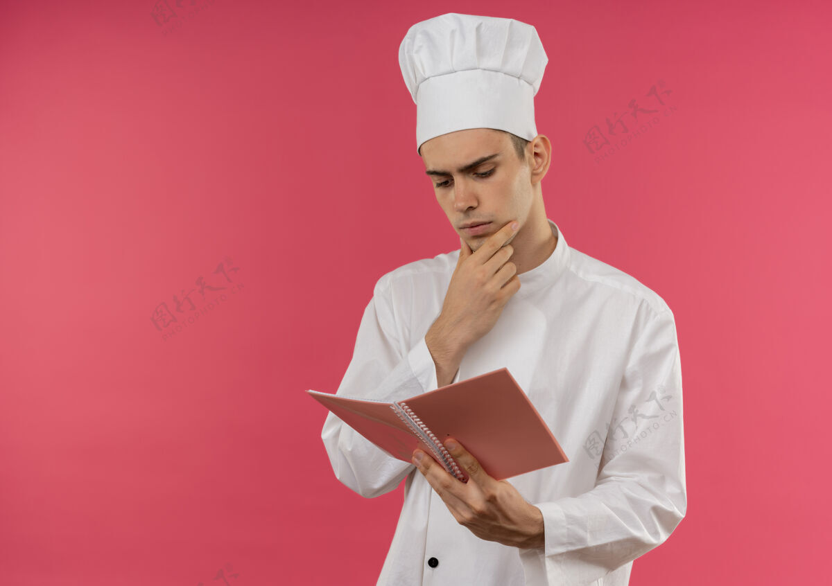 手想着年轻的男厨师穿着厨师制服拿着书看着noyebook手放在下巴上留着复印空间厨师厨师下巴