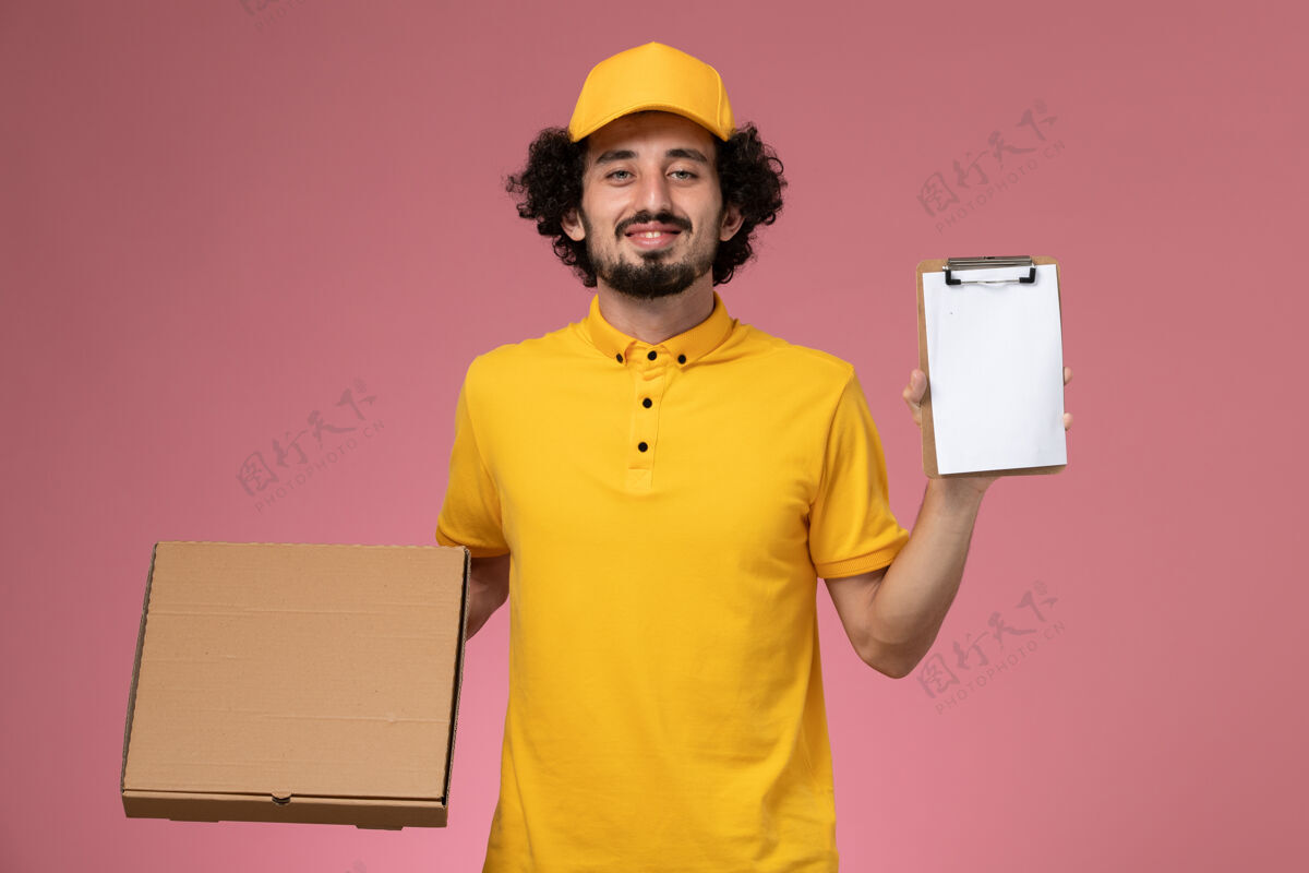 黄色正面图穿着黄色制服的男快递员拿着食品快递箱和笔记本放在粉红色的墙上正面持有男人