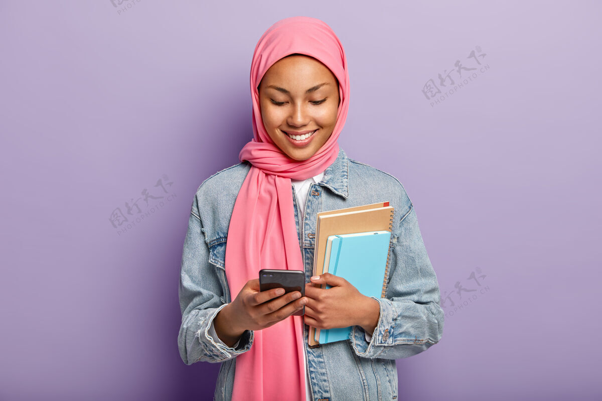 日记高兴的穆斯林女学生在社交网络中查看照片 持有现代手机 观看有趣的视频内容手机打字移动