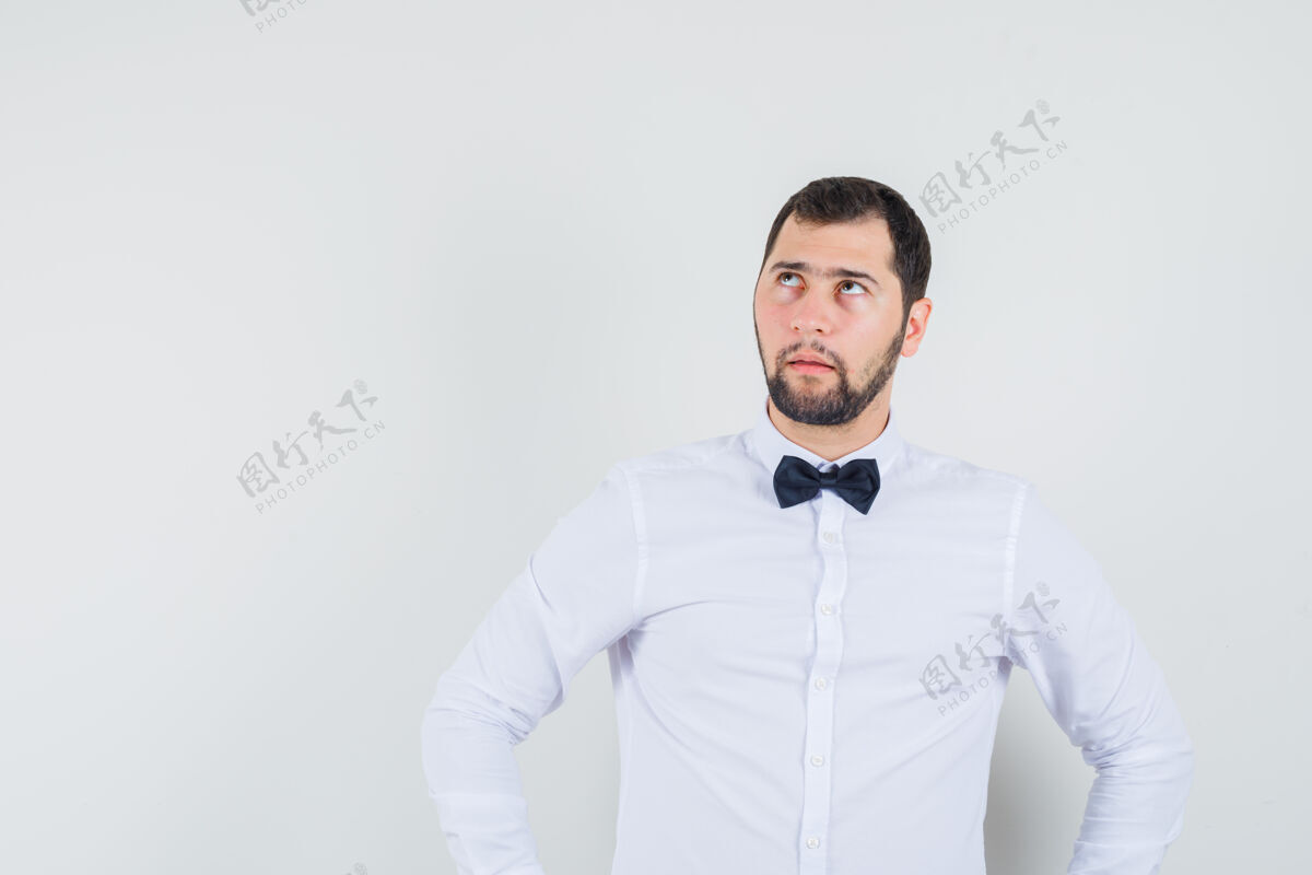 严肃年轻的男性手放在腰上 穿着白衬衫 面带沉思 仰望前方自信肖像休闲