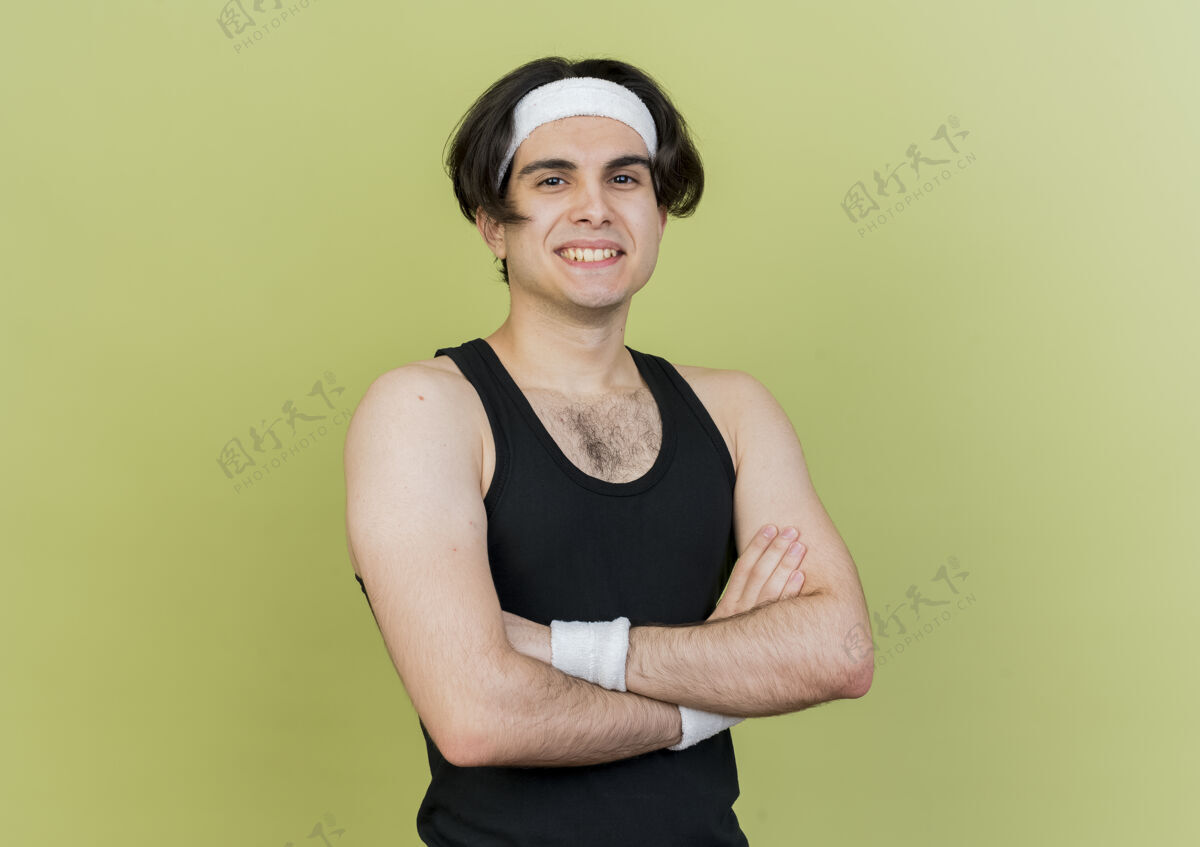 交叉年轻的运动型男子 穿着运动服 戴着头巾 胸前交叉着双臂 自信地微笑着手臂看微笑